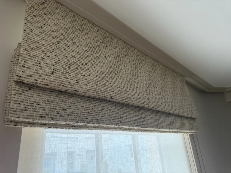 Roman blind in a flecked boucle-style weave raised above a sheer blind, seen from below