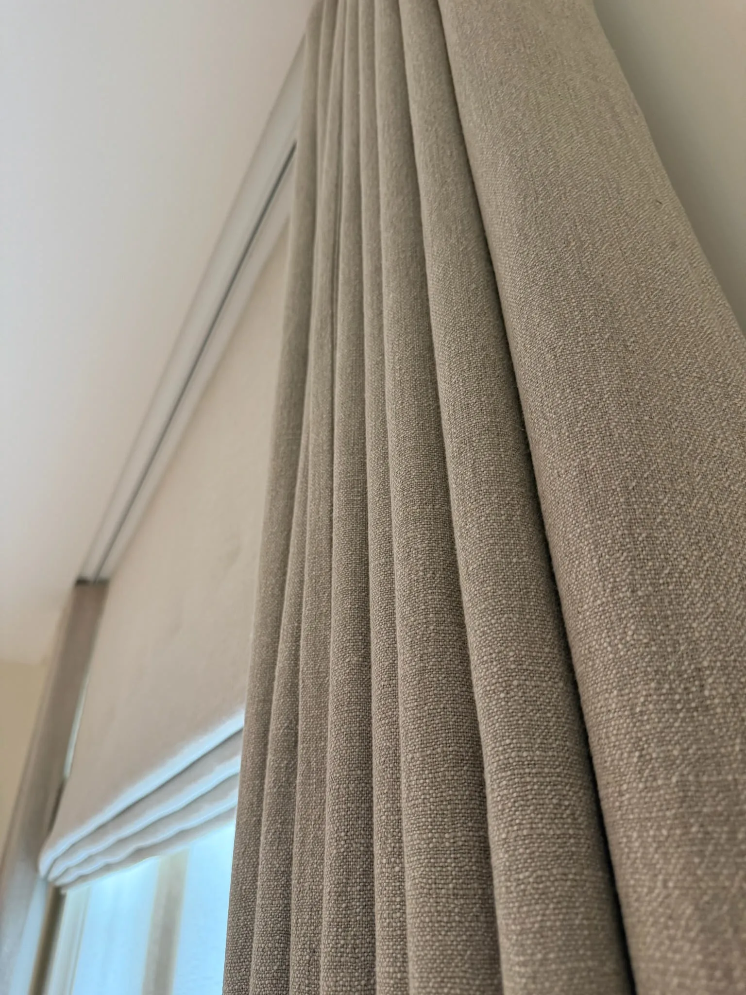 Neutral textured curtain on a ceiling track, with a pale blind in the window recess behind