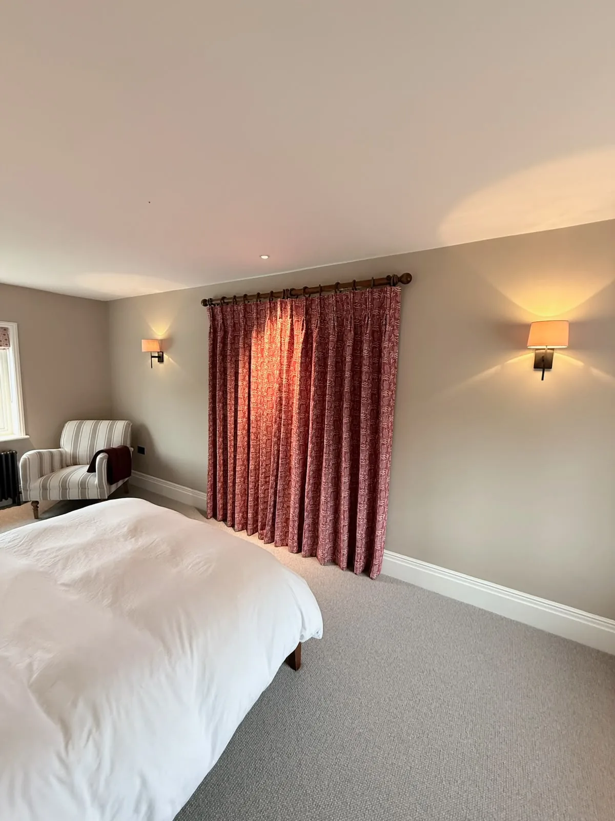 Bedroom with red patterned curtains drawn on a wooden pole between two wall lights