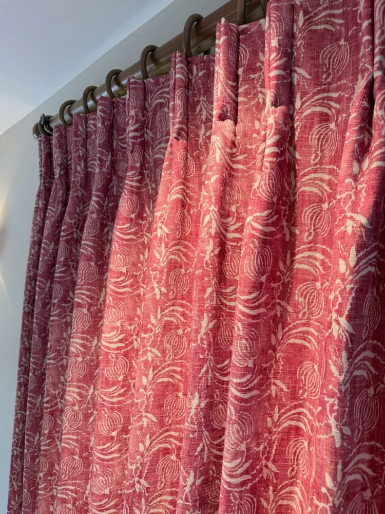 Red and white patterned pinch-pleat curtain on rings, lit by sunlight