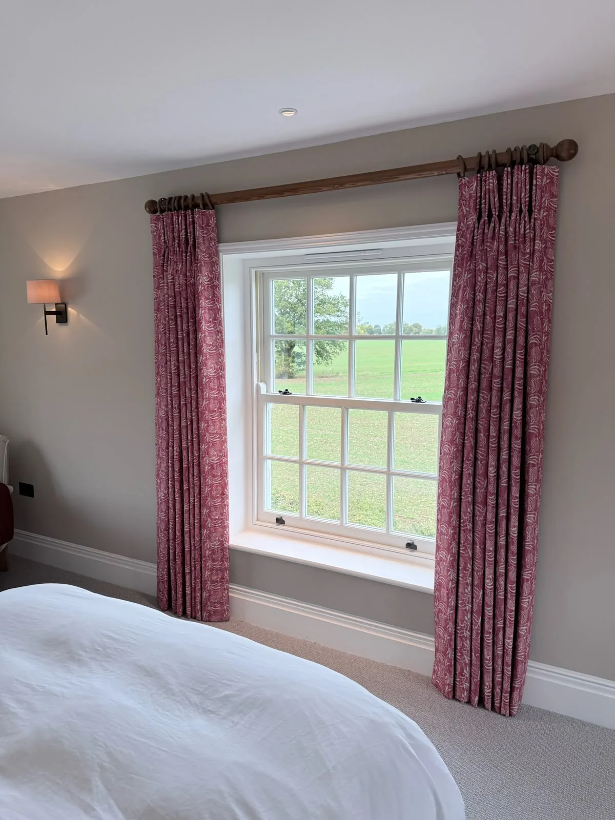 Red patterned curtains framing a sash window beside a wall light