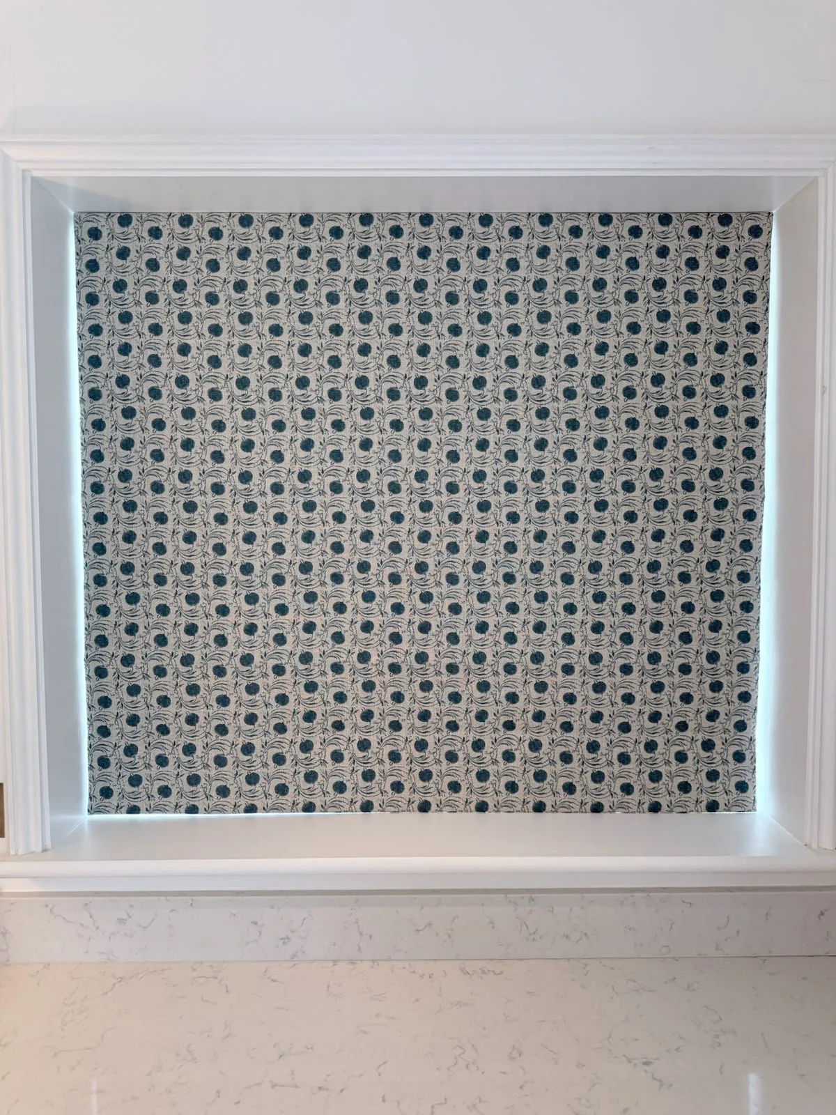 Roman blind in a teal and grey geometric spot print, lowered in a white window recess