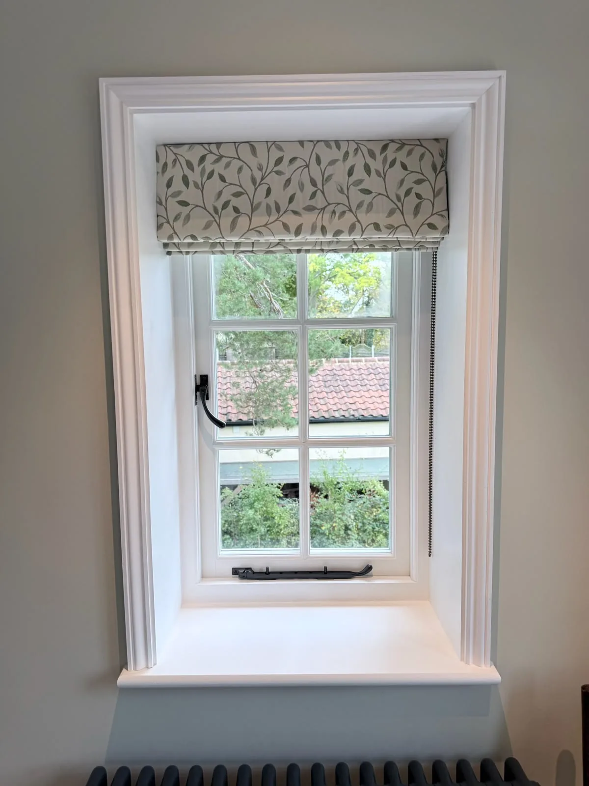 Trailing-leaf print Roman blind raised in a deep casement window with an architrave