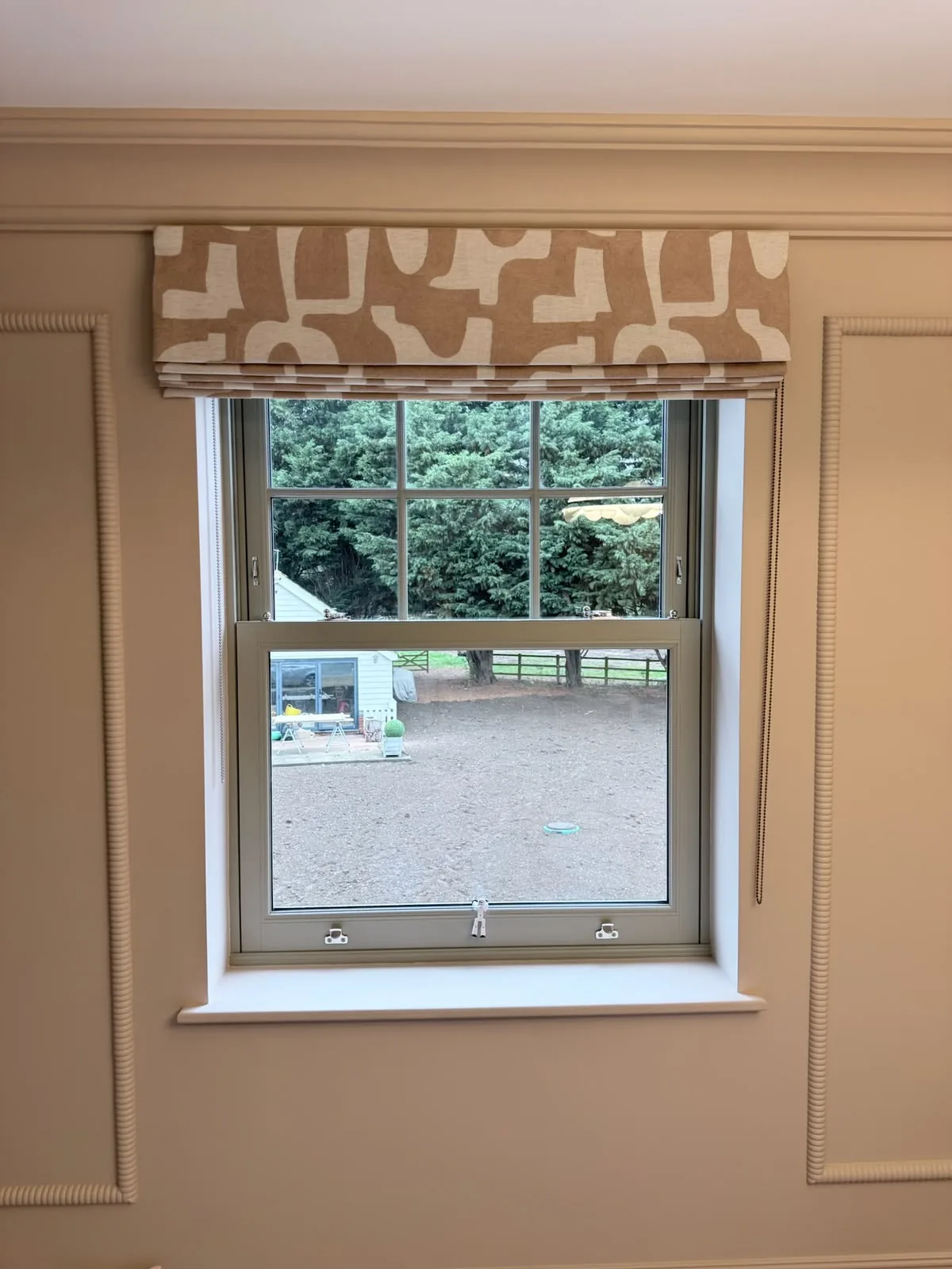 Roman blind in a bold tan and white geometric print above a sash window in a panelled room