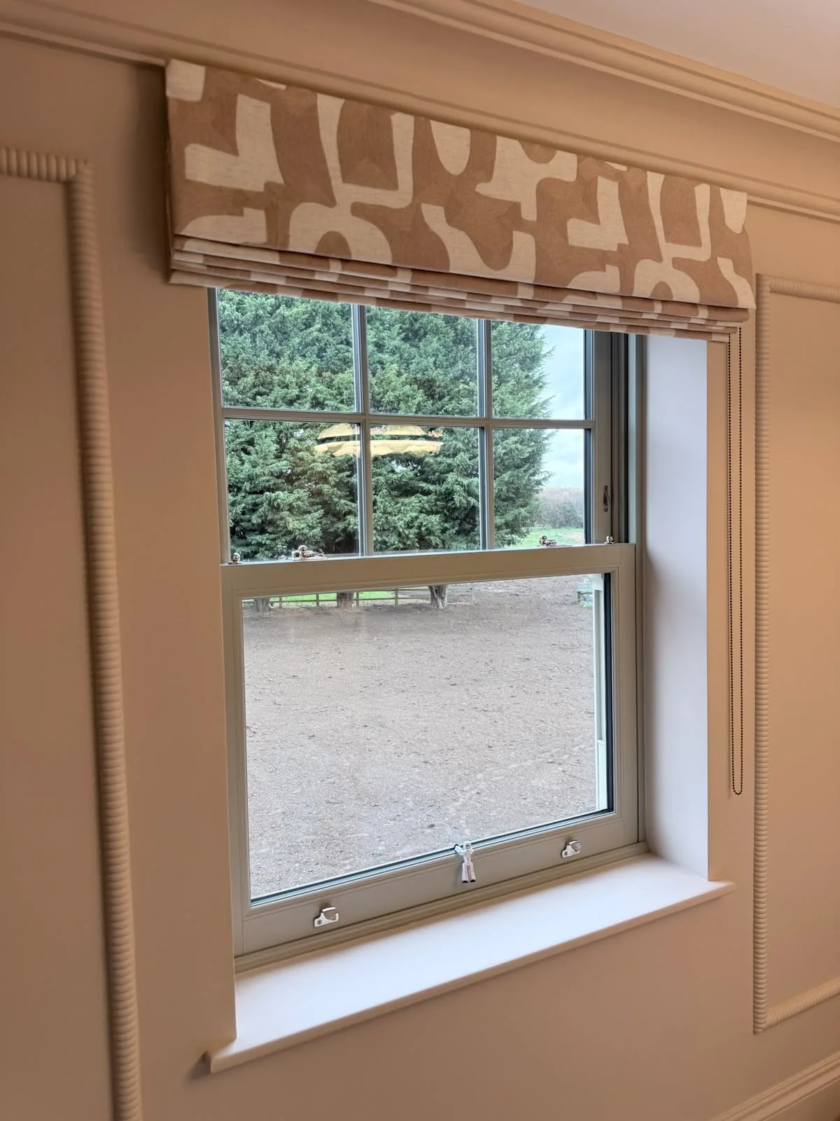 Tan and white geometric-print Roman blind raised above a sash window set in a panelled wall