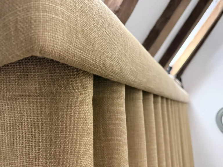 Close-up of a fabric-covered pelmet above mustard linen-look wave curtains, under oak beams
