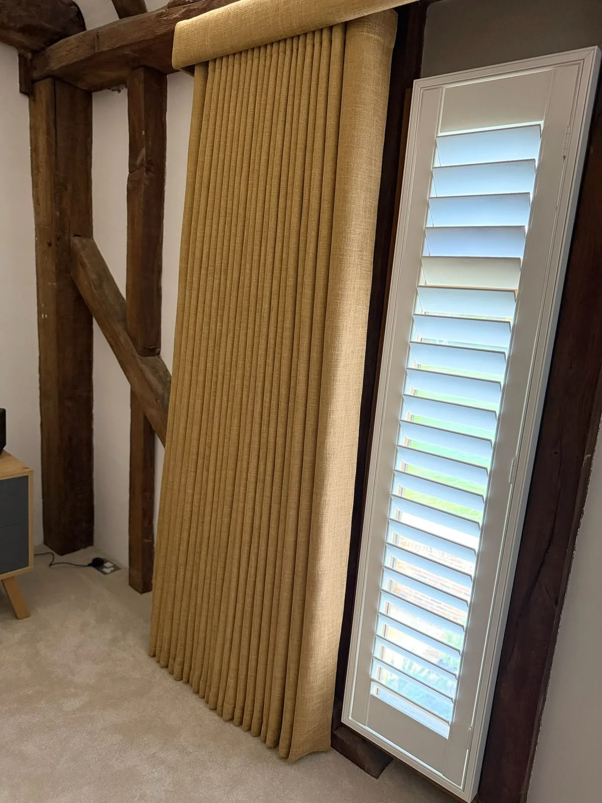 Mustard linen-look curtain stacked beside a full-height shuttered window between oak posts