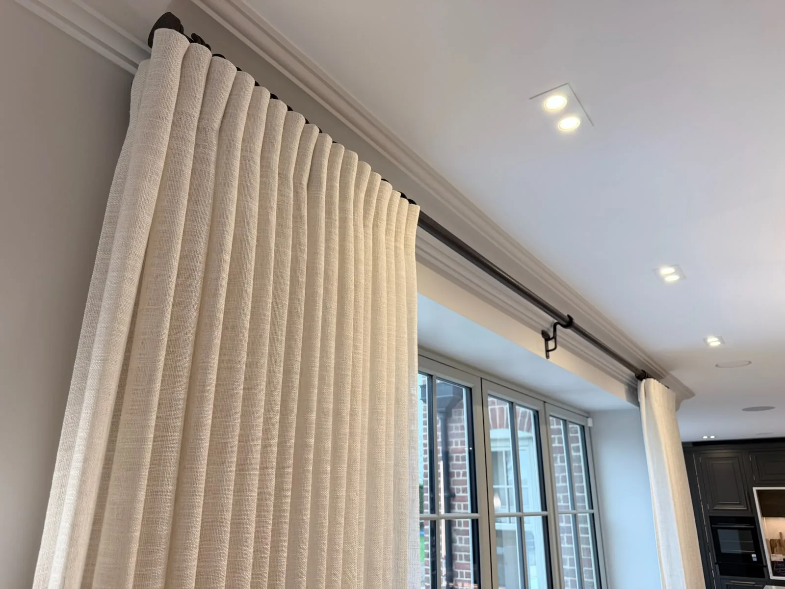 Looking up at cream curtains on a dark metal pole running across wide glazed doors