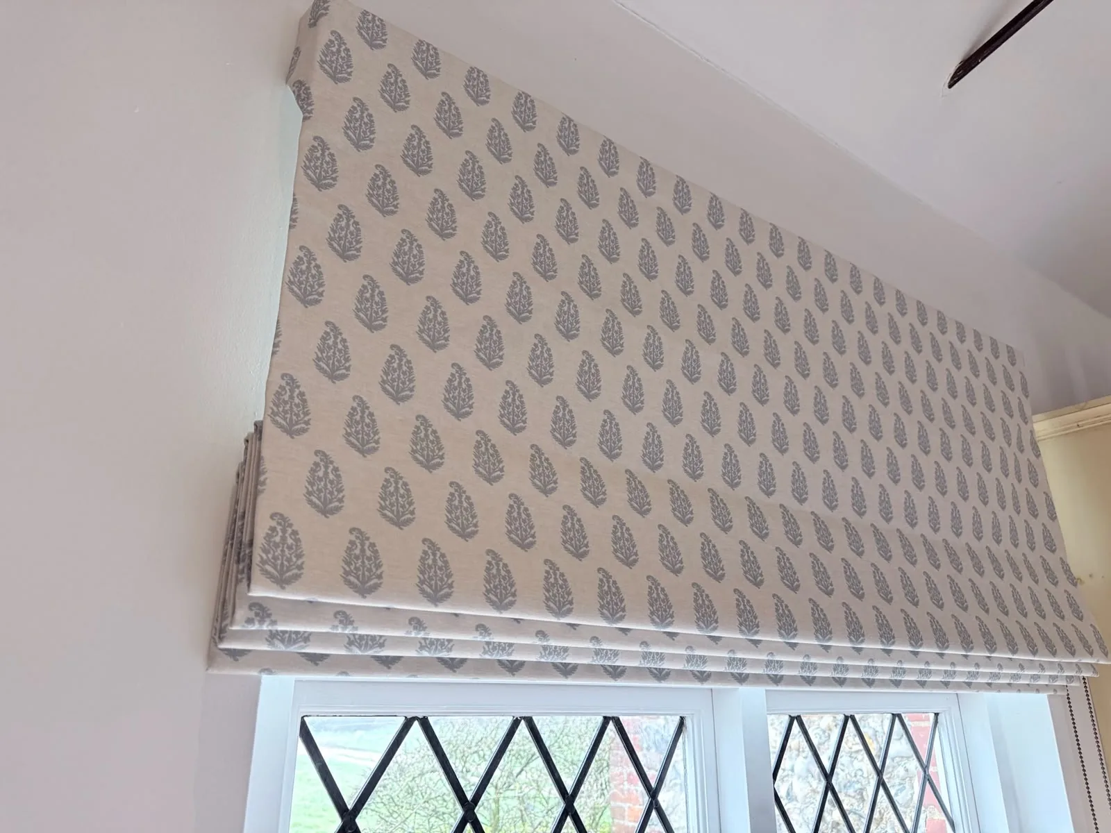 Roman blind in a small grey leaf motif, raised above a leaded diamond-pane window