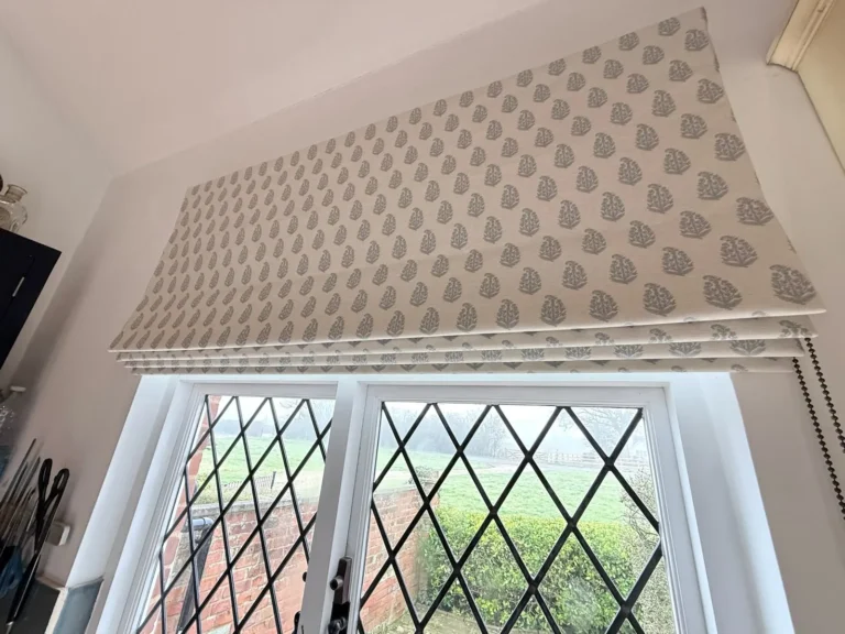 Grey leaf-motif Roman blind raised above leaded diamond-pane casement windows
