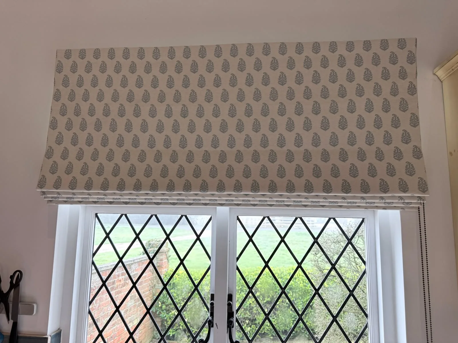 Front view of a grey leaf-motif Roman blind raised above leaded diamond-pane windows