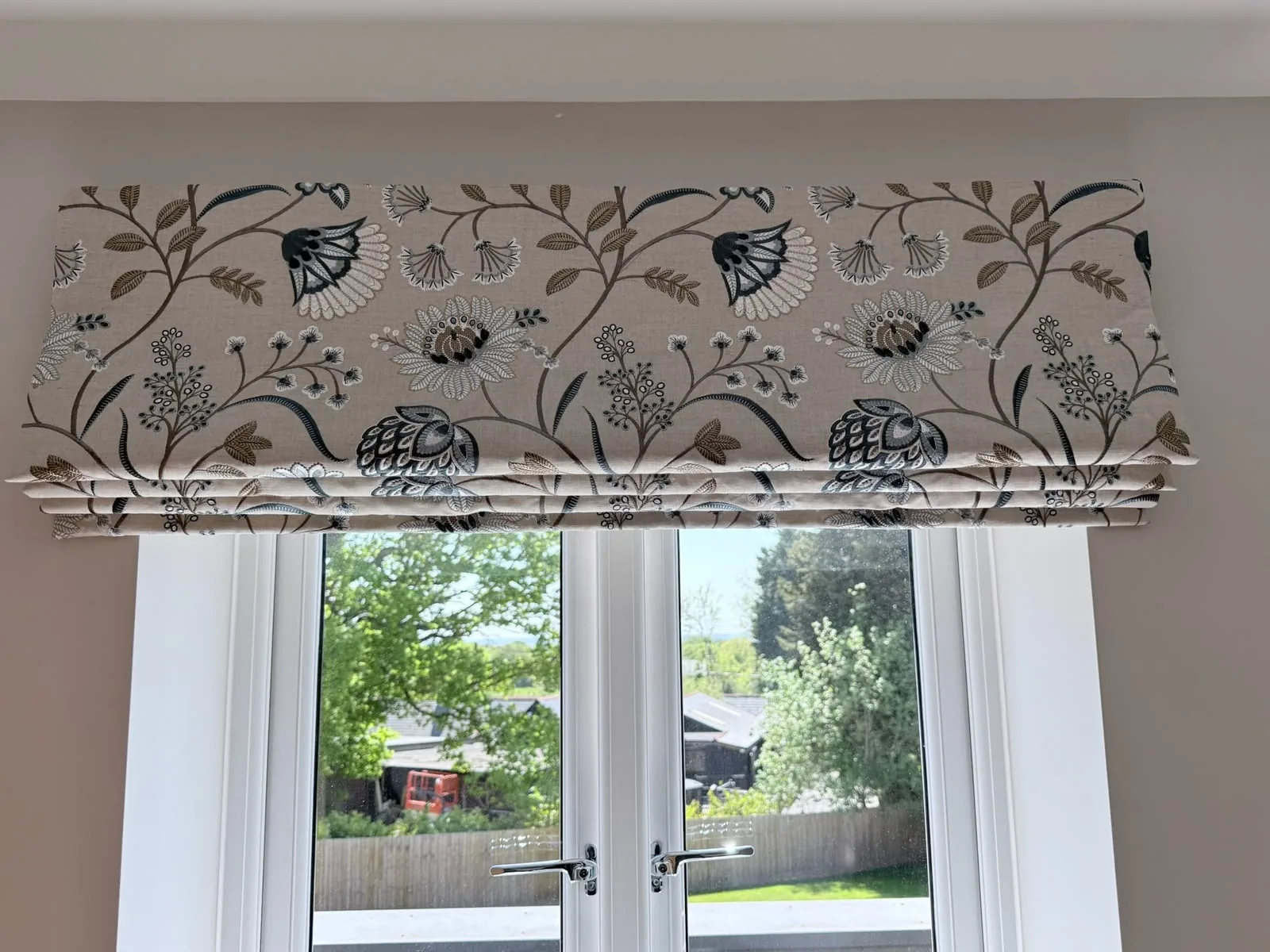 Roman blind in an embroidered-look botanical print, raised above French doors overlooking a garden