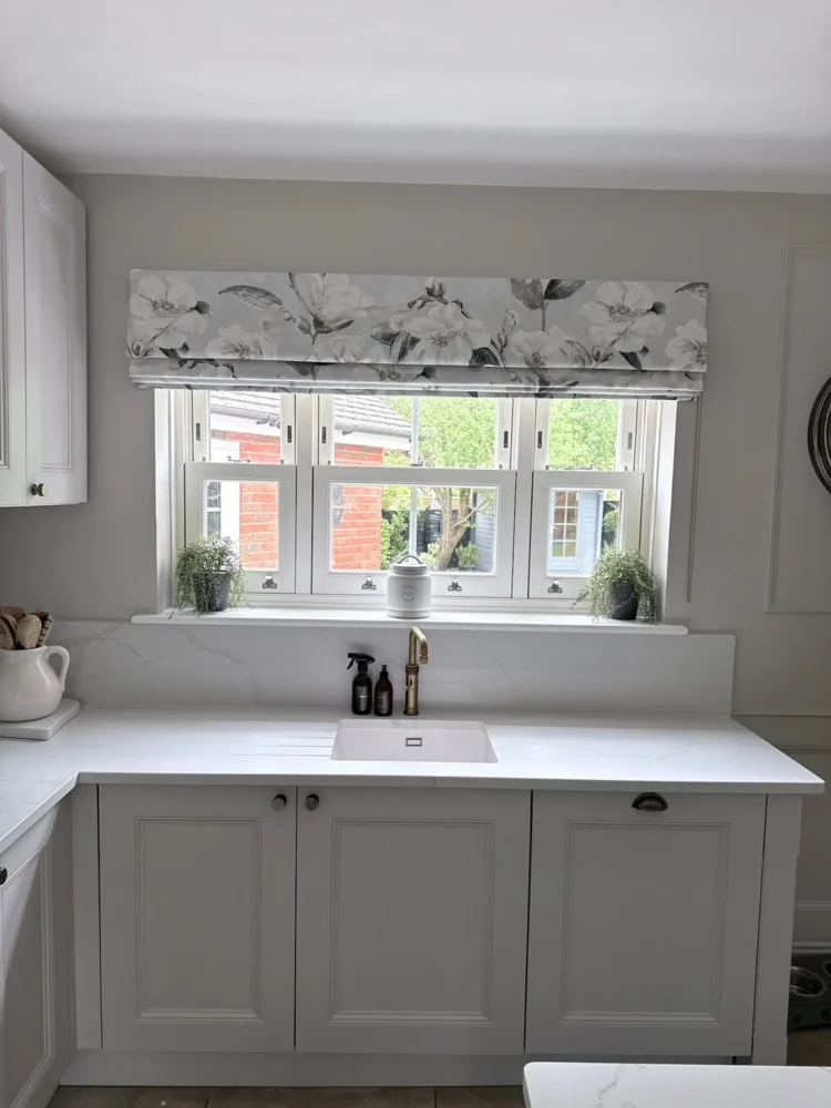 Floral Roman blind raised above a window over a white kitchen sink run