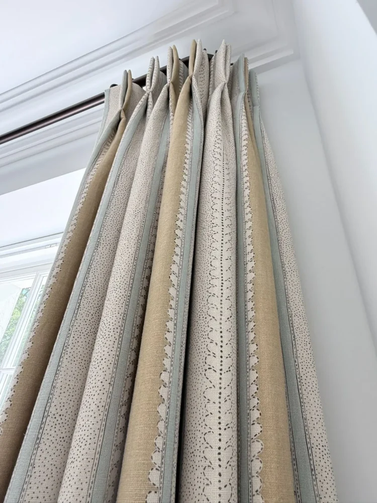 Looking up at pinch-pleat curtains in a neutral striped and spotted fabric on a dark pole