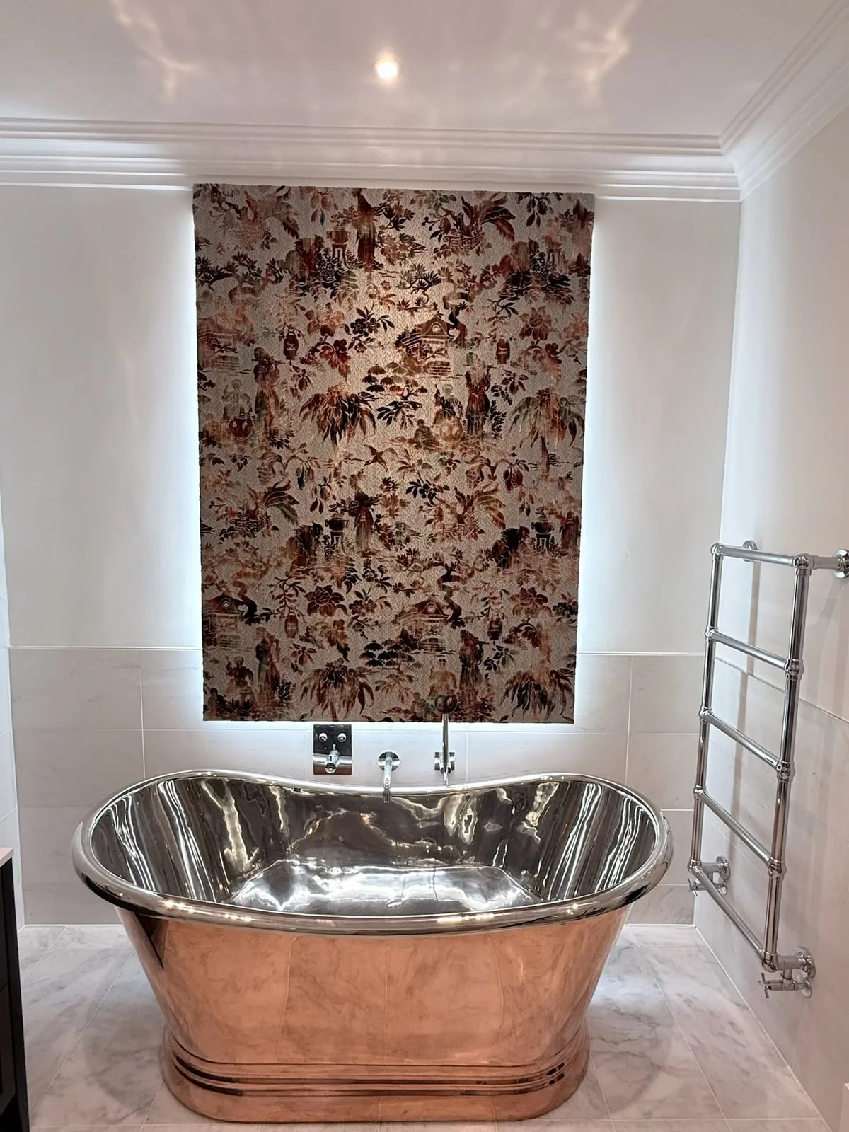 Rust floral Roman blind lowered at a backlit window behind a copper roll-top bath