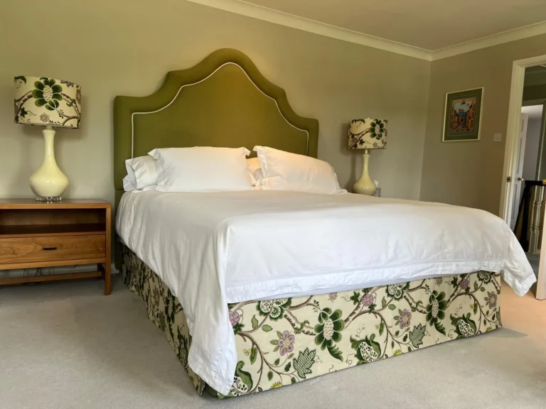 Bedroom with a shaped olive velvet-look headboard with contrast piping, a floral crewel-style bed valance and floral lampshades
