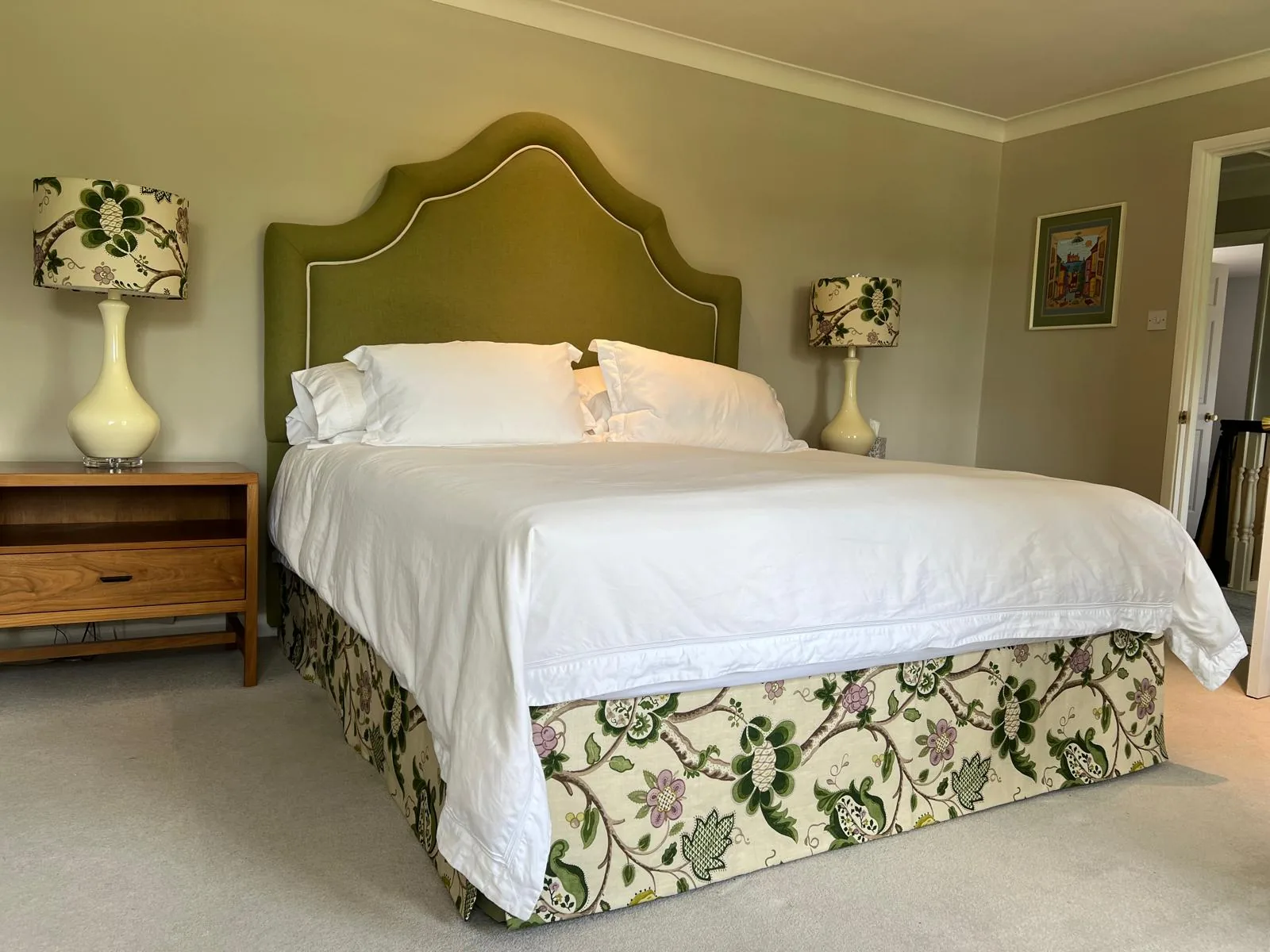 Bedroom with a shaped olive velvet-look headboard with contrast piping, a floral crewel-style bed valance and floral lampshades