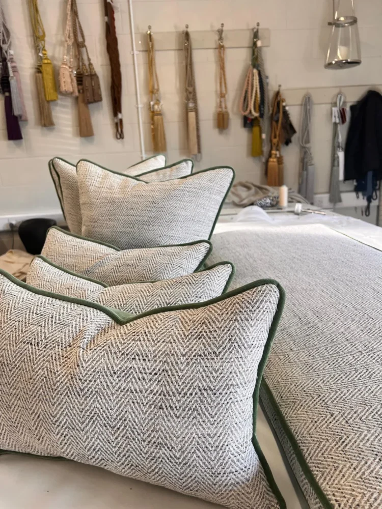 Herringbone cushions with green piping lined up in the workroom, with tassel tiebacks on the wall behind