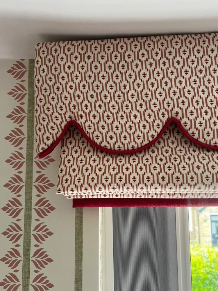 Scalloped pelmet and Roman blind in a red geometric print with red velvet trim, beside leaf-print curtains