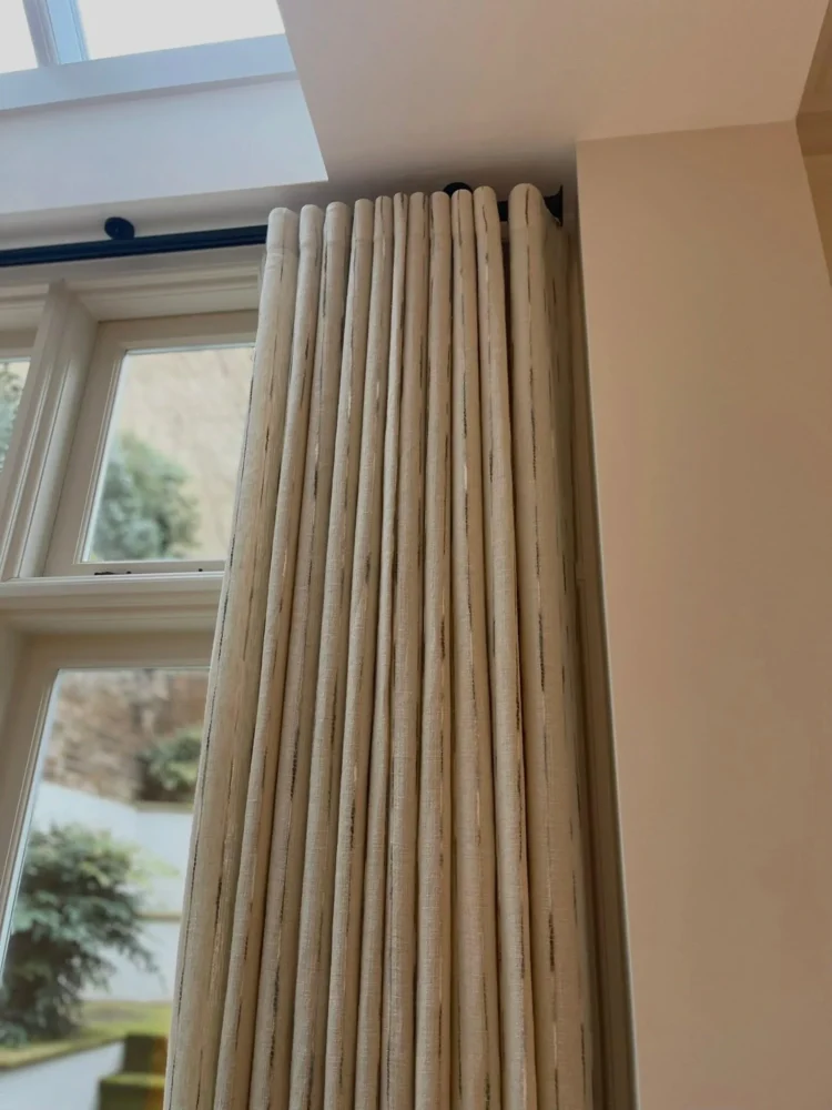 Neutral textured curtain with a tall pleated heading, stacked beside a window