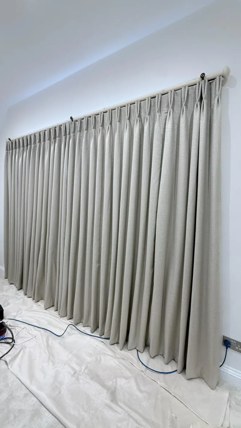 Long run of grey pinch-pleat curtains on a pole, hung over dust sheets during fitting