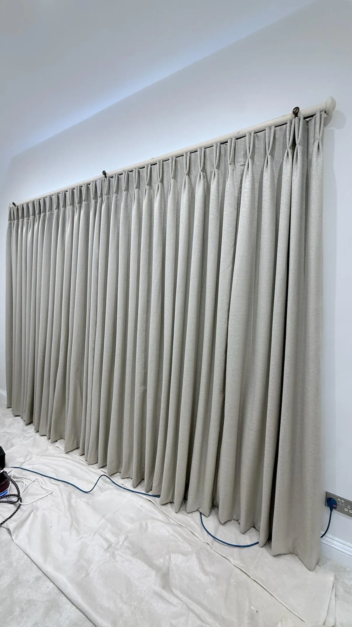 Long run of grey pinch-pleat curtains on a pole, hung over dust sheets during fitting