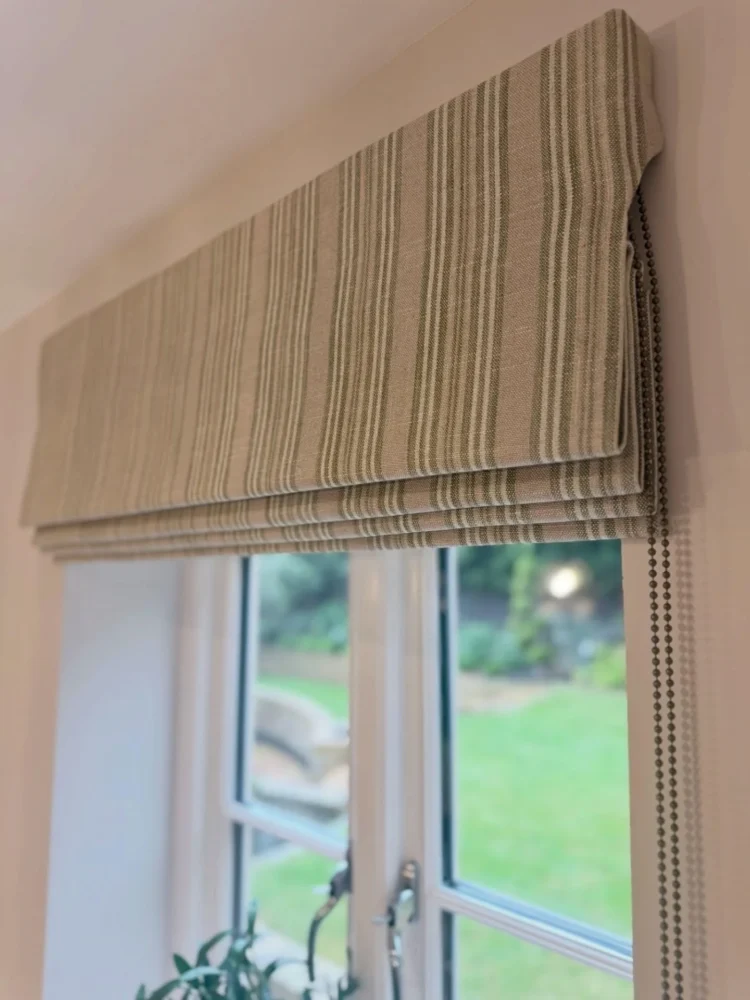 Striped Roman blind with a beaded chain raised above French windows onto a garden