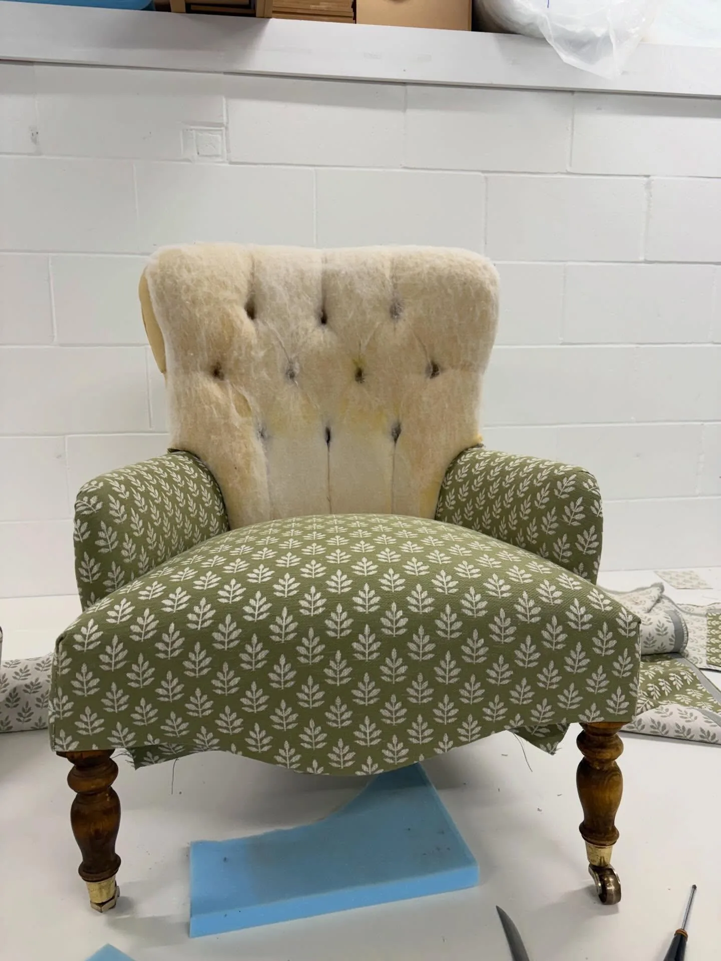 Chair being reupholstered in a green leaf print in the workroom, with its old wool back still in place