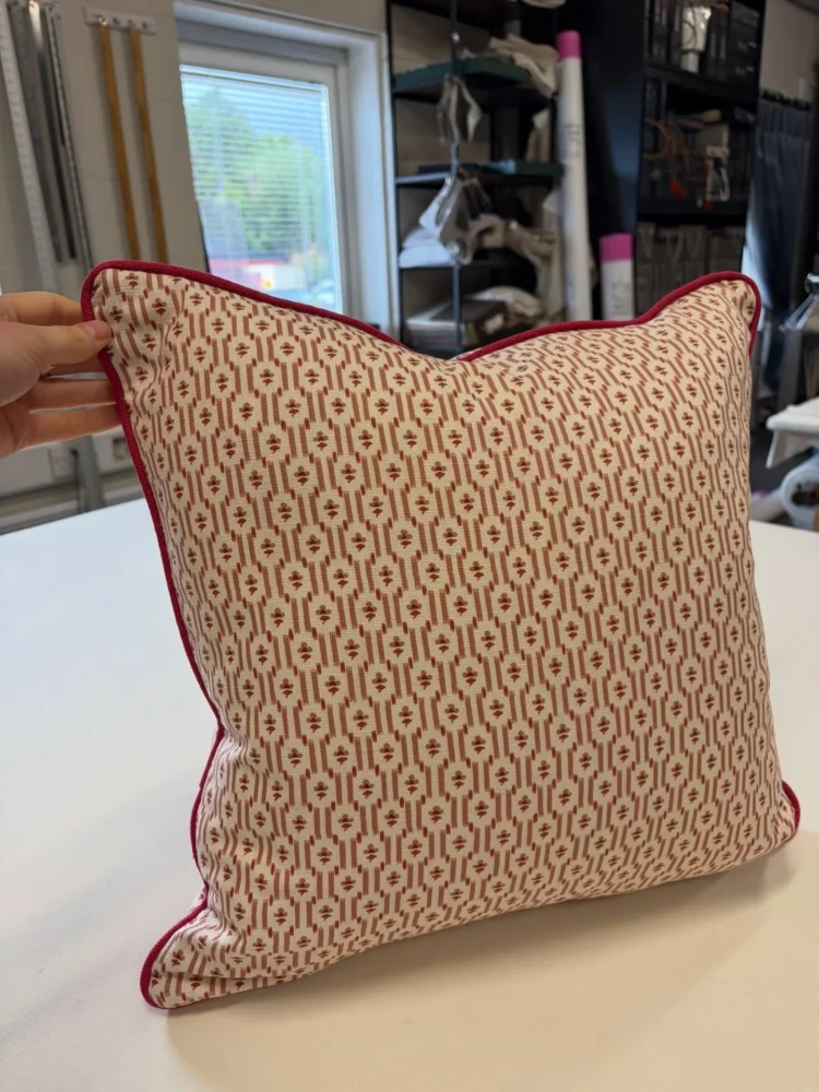Red and cream geometric cushion with red piping, held up in the workroom