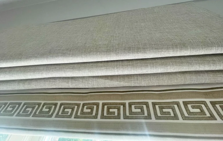 Close-up of the stacked folds of a neutral Roman blind finished with a Greek key border