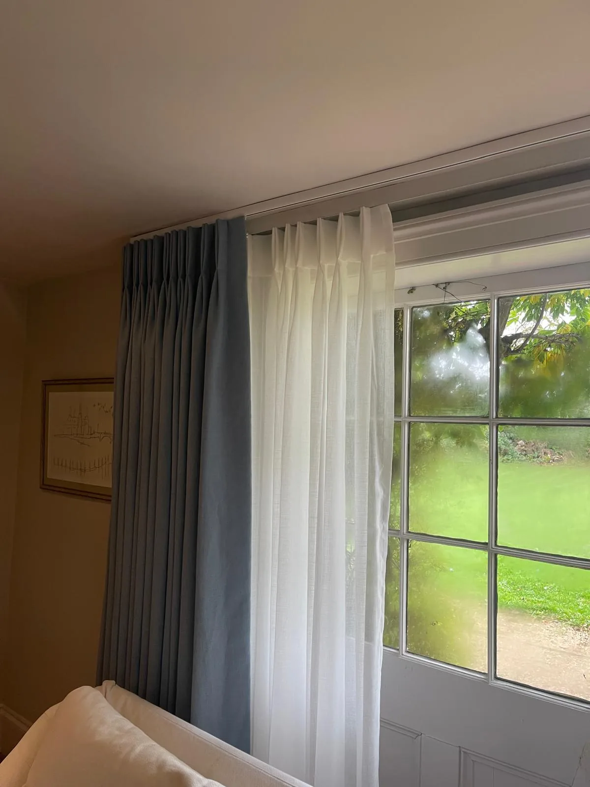 Blue-grey dress curtain and sheer voile at a window overlooking a garden