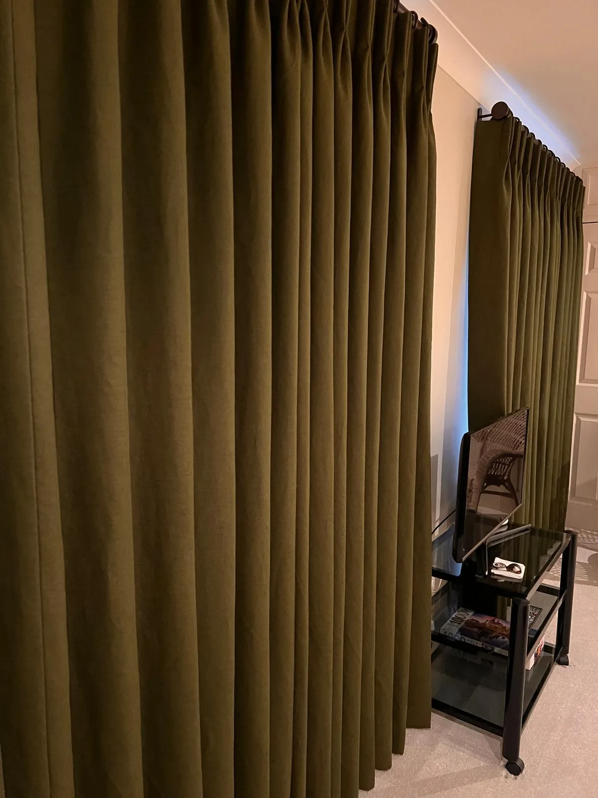 Olive velvet pinch-pleat curtains drawn along a wall beside a black side table