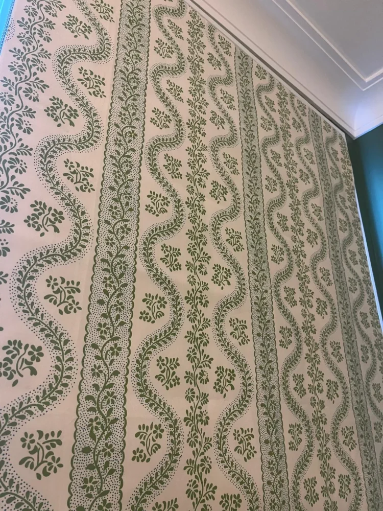 Green and white trellis-print Roman blind lowered at a window below a cornice