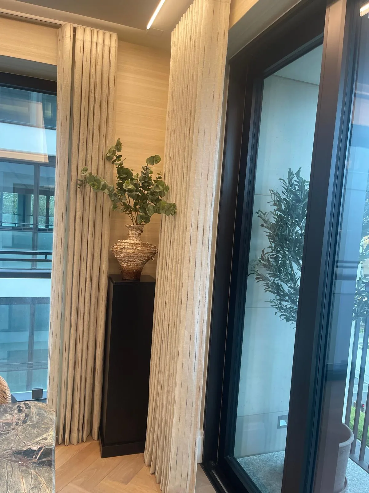 Striped textured curtains on a ceiling track beside black-framed full-height glazing and a plant