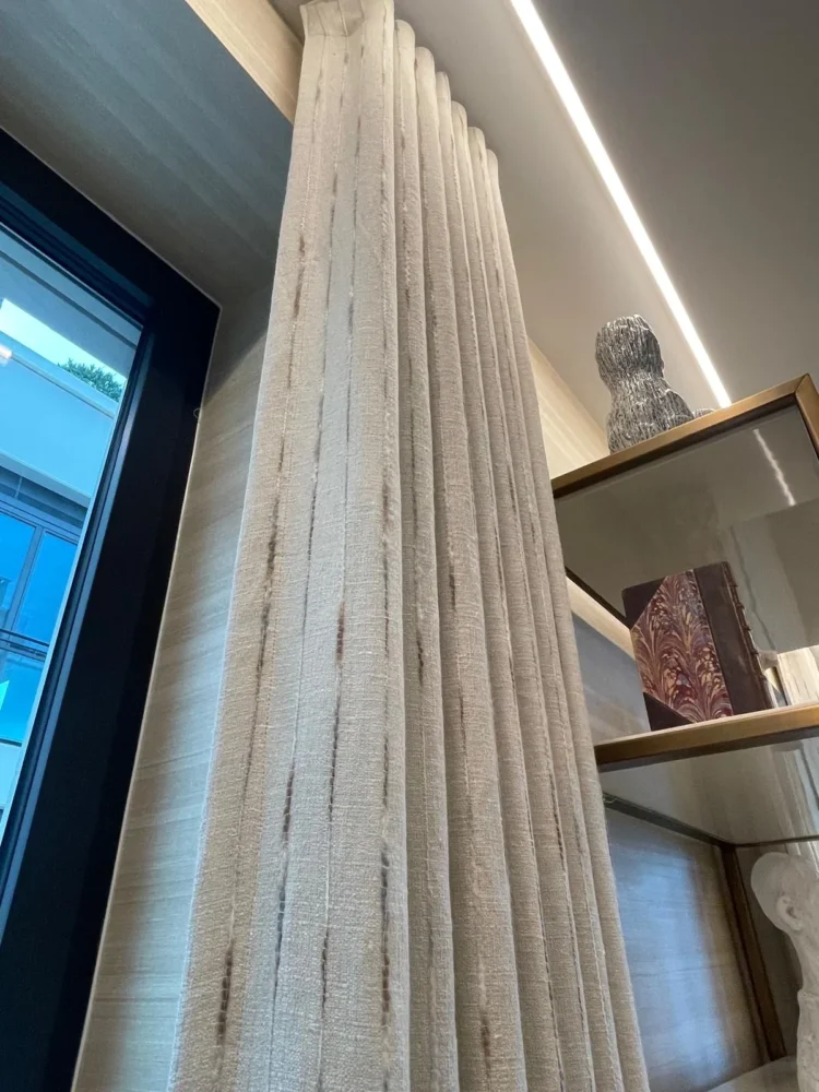 Looking up a striped textured curtain beside black-framed glazing and display shelves