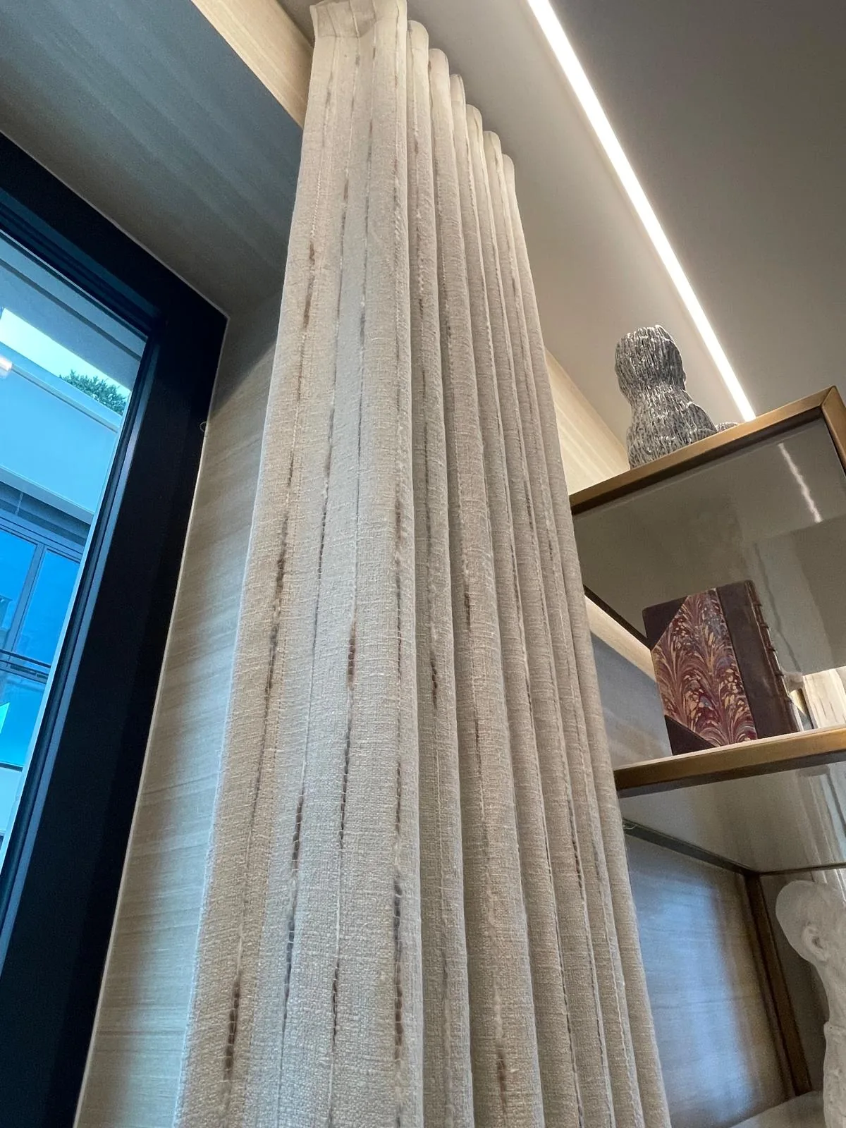 Looking up a striped textured curtain beside black-framed glazing and display shelves