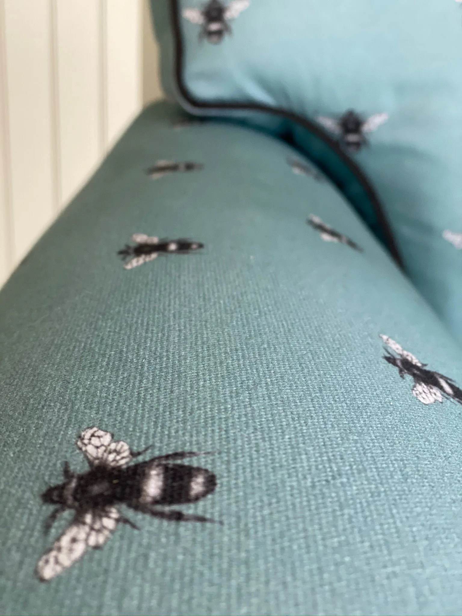 Close-up of the arm of a chair in a duck-egg bee-print fabric with dark piping
