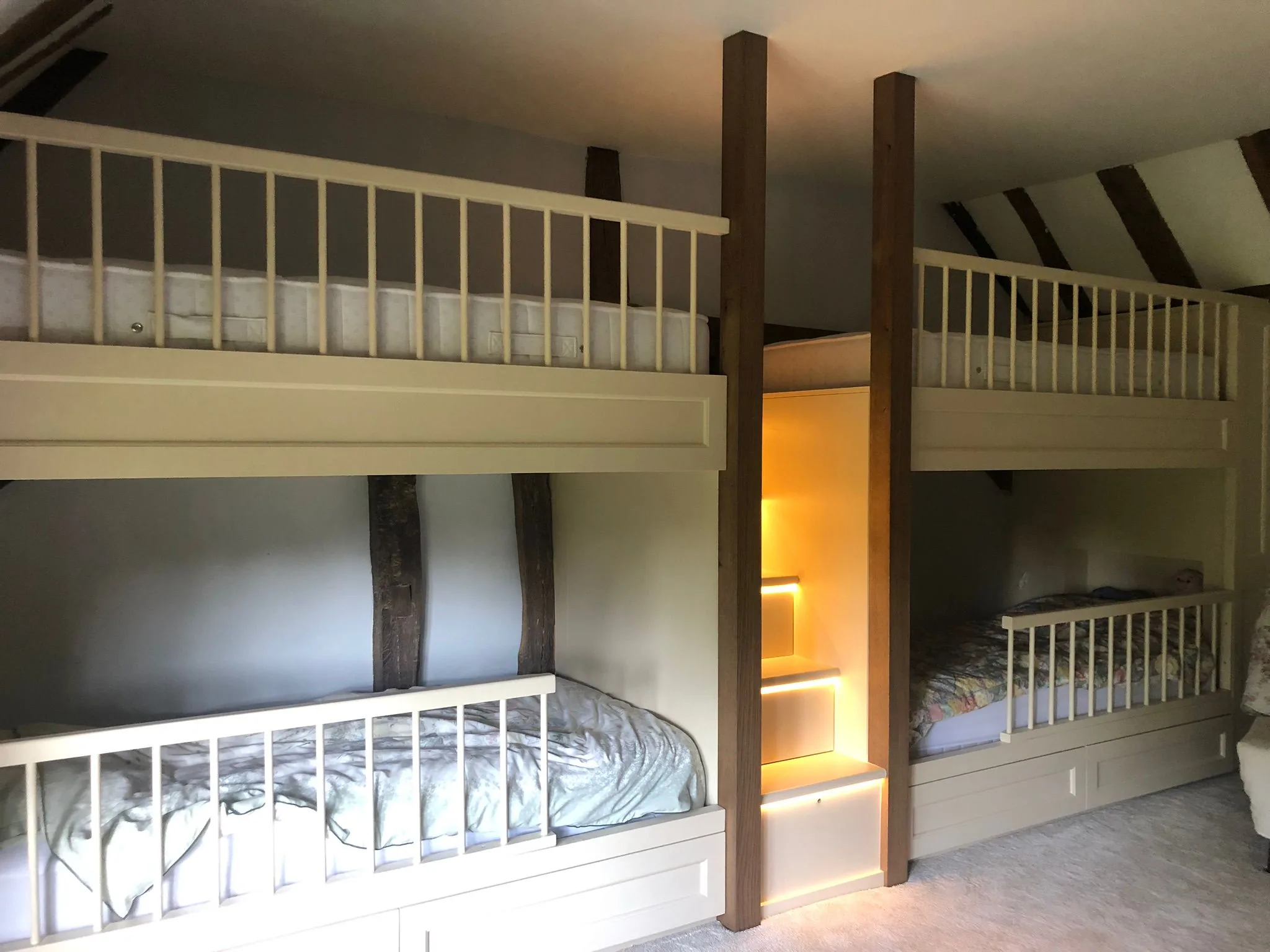 Finished built-in painted bunk beds with oak posts, rails and lit steps under a beamed roof