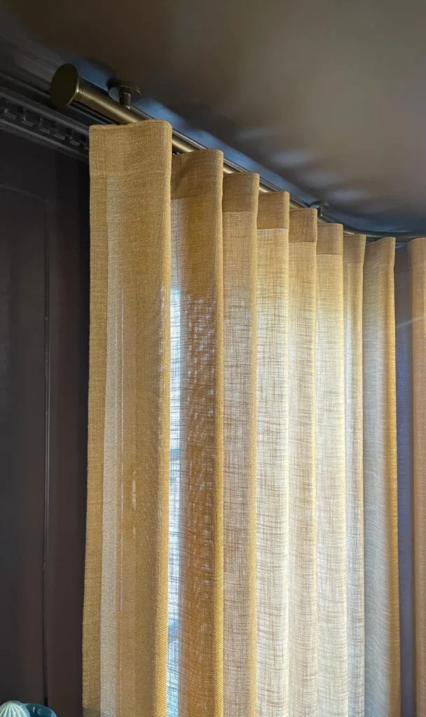 Gold sheer wave curtain hung from a bronze pole against a dark-painted wall