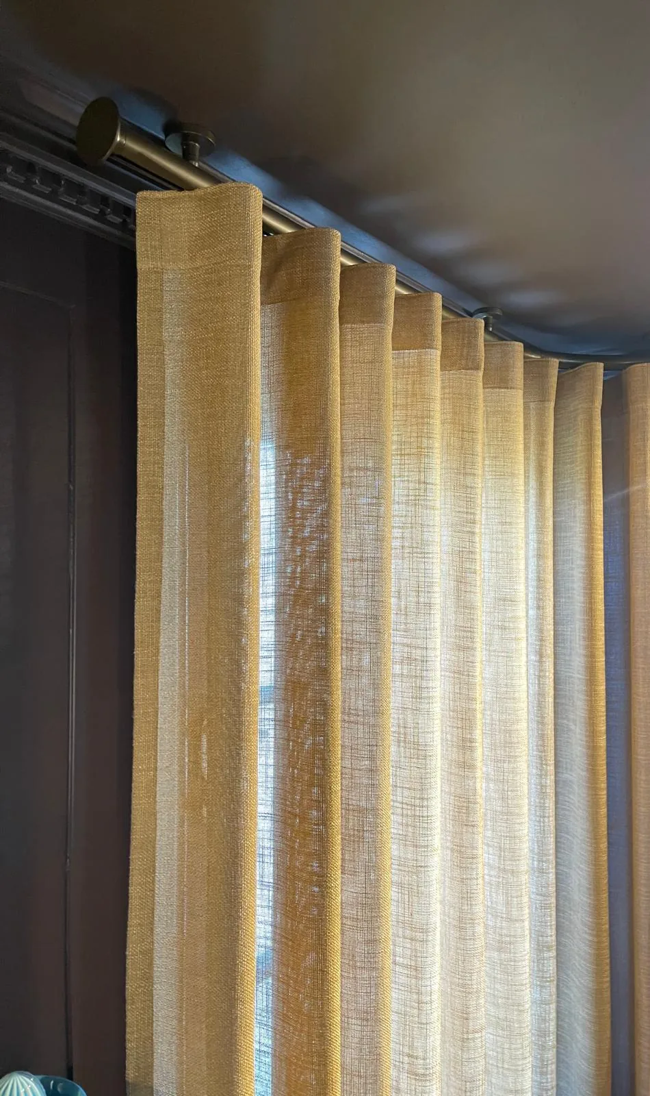 Gold sheer wave curtain hung from a bronze pole against a dark-painted wall