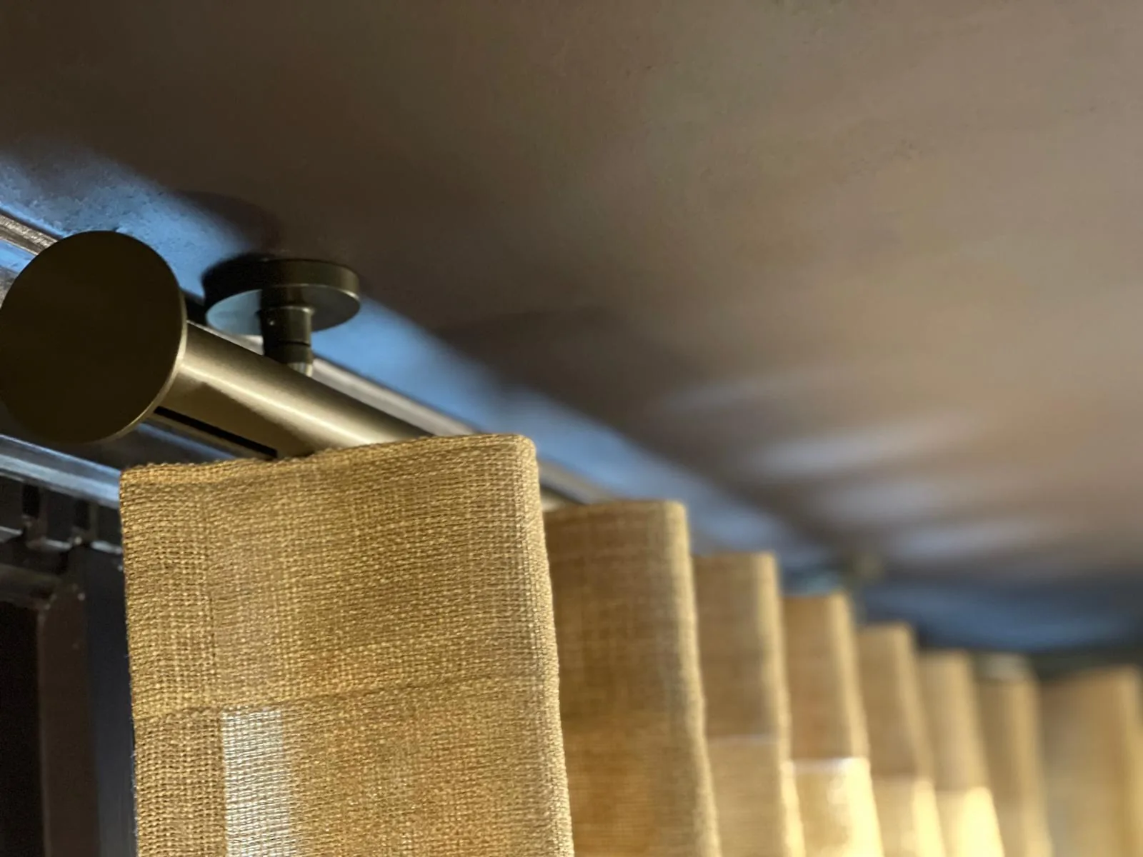 Close-up of a bronze pole and end cap with a gold curtain heading below