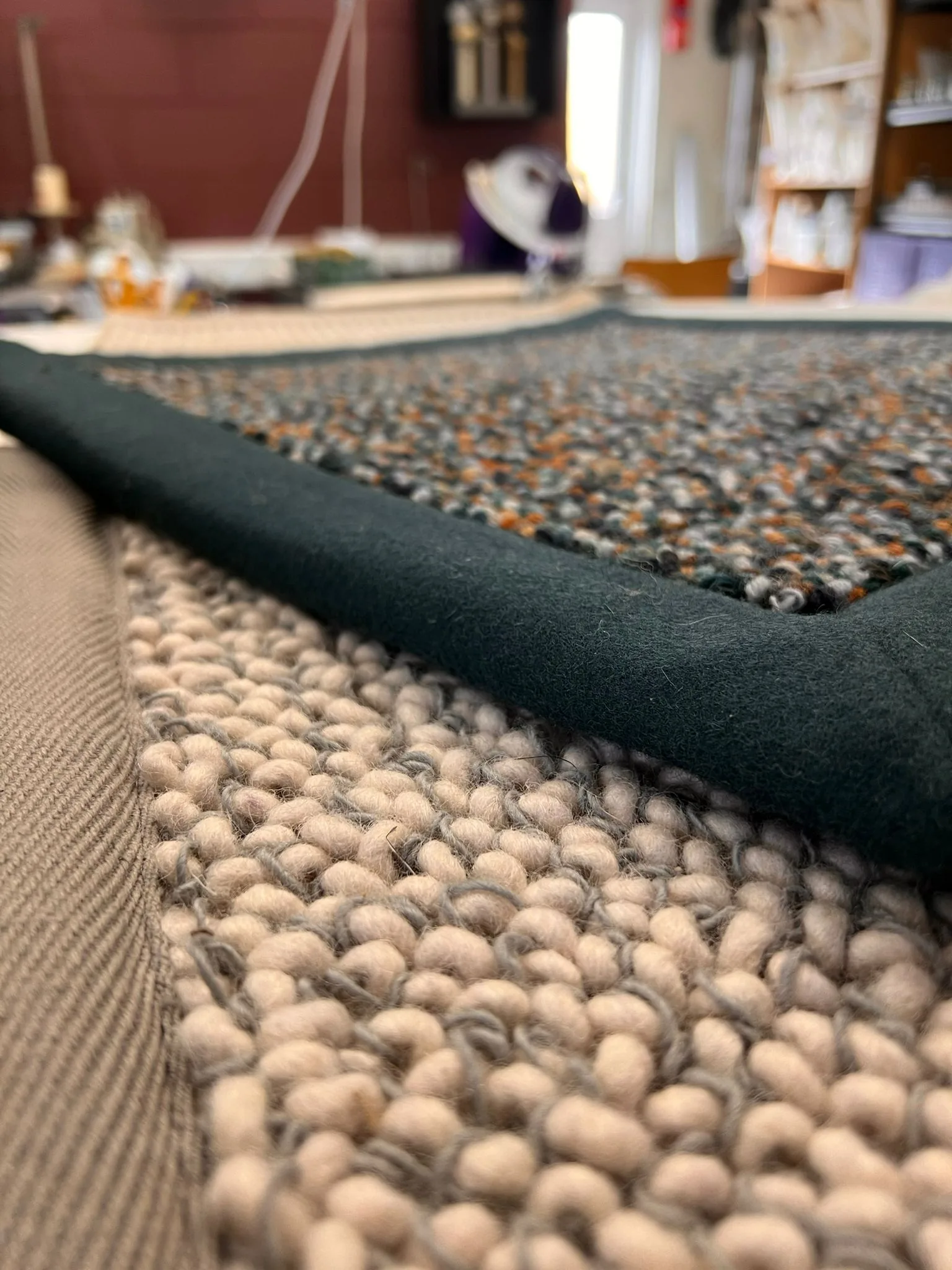 Close-up of a flecked wool rug sample with a dark green bound edge